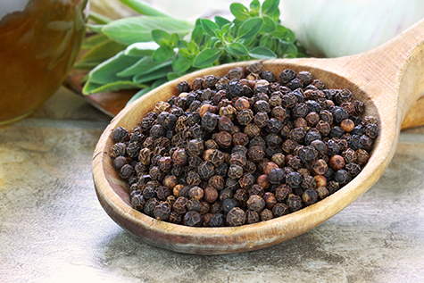 A wooden spoon full of peppercorns on a kitchen counter