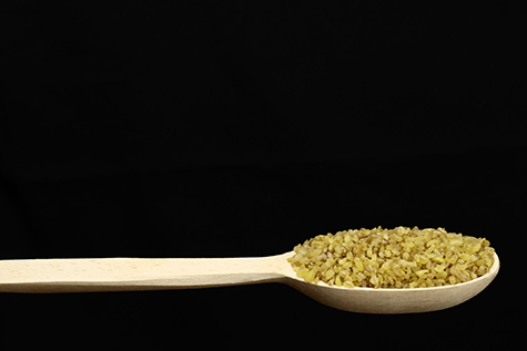 bulgur wheat grain in wooden spoon on black background. Vegan healthy food