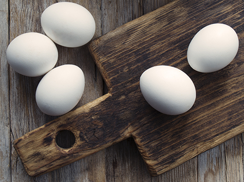 White eggs and a cutting board on a wooden table.
