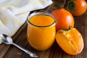 Puree with persimmon in the glass jar on the wooden background