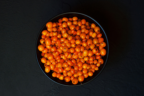 Sea buckthorn. Ripe fresh berries in bowl on black concrete background. Top view