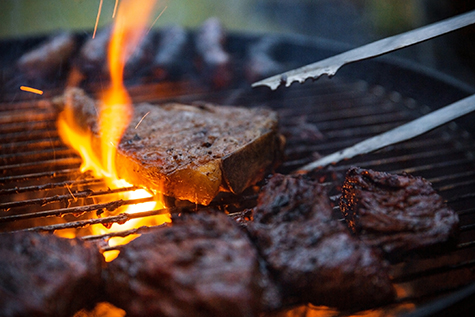 Flame Grilled Steaks Being Flipped On Barbecue With Tongs