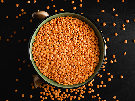 Bowl with seeds of red lentils on a black stone background. Lentil seeds and cloves of garlic are scattered next to the bowl. Flat lay