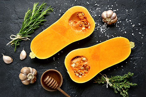 Halves of raw organic butternut squash with spices and ingredients for making