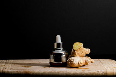 Bottle of cosmetics with ginger oil extract on wooden board with ginger roots. Black background, copy space.