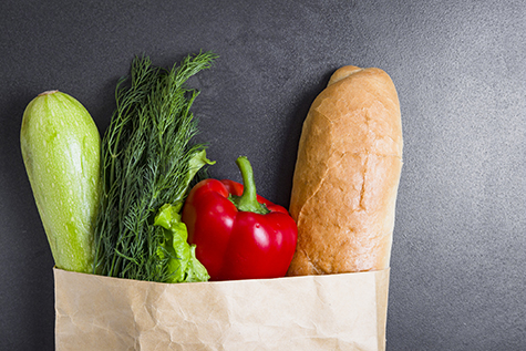 Vegetarian purchases at grocery store. Vegetables in paper bag on black background. Healthy food concept. Pack with vegetables. Zucchini, dill, greens, baguette, pepper.