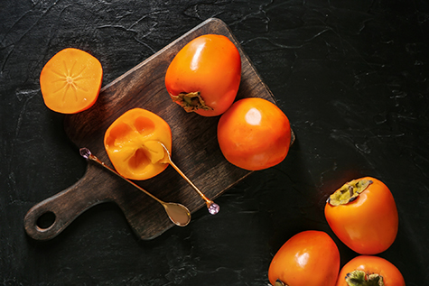 Wooden board with ripe persimmons on table, top view