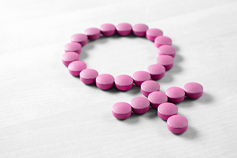 Medicine for woman. Menopause, pms, menstruation or estrogen concept. Female health. Gender symbol made from pink red pills or tablets on wooden table.