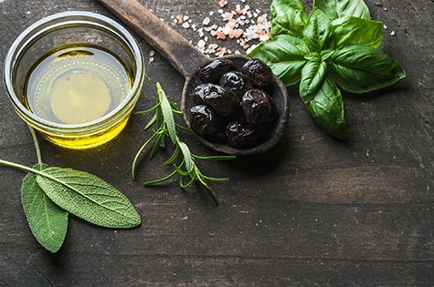 Greek black olives, fresh herbs and oil on dark rustic wooden background