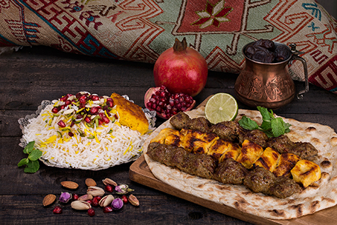 Traditional Middle eastern Persian chicken and lamb meat Shashlik Kebab (skewered meat) BBQ Grill on flat pita bread and saffron rice and tahchin and pomegranate on a dark background. Iranian cuisine