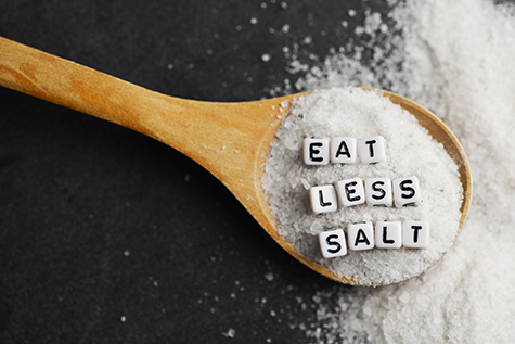 Eat less salt advice written with plastic letter beads on granulated salt – healthy food lifestyle