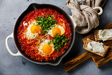 Breakfast Shakshuka Fried eggs with tomatoes in frying pan and bread with soft goat cheese