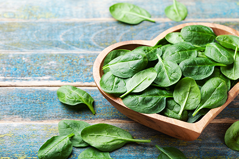 Baby spinach leaves in bowl on wooden table. Organic and healthy food.