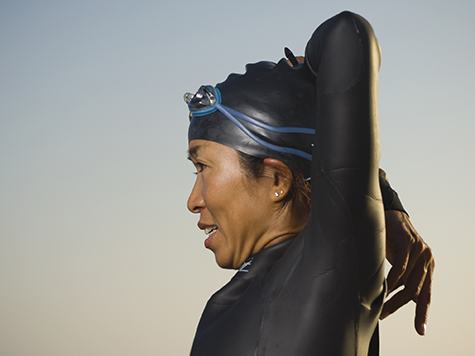 Asian woman stretching in wetsuit and goggles