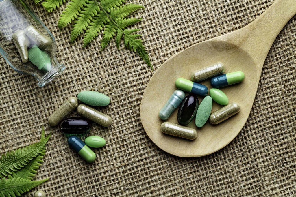 Close up of assorted capsules and pills into wooden spoon on a rustic background