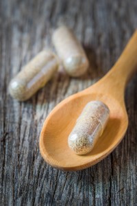 Herb capsules spilling in wooden spoon.