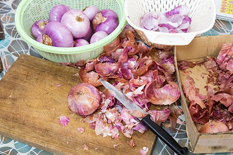 Onion skin being prepared peeled with knife, chopping board colander
