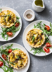 Vegetarian savory hands pie with porcini mushrooms, leeks, potatoes and arugula, tomatoes salad on grey background, top view. Mediterranean style lunch, snack, appetizer, breakfast